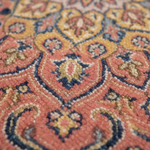 Close-up of a traditional patterned rug with coral pink, mustard yellow, navy blue, and beige woven detailing.