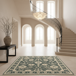 A large rectangular area rug with a traditional floral pattern in muted teal and cream is displayed on a light-colored staircase landing in a grand, elegant interior with a spiral staircase and arched windows.