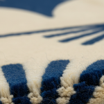 Close-up of a textured rug with deep blue and cream stripes and fringe, showing the detailed pile and fibers.