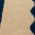 Close-up of a textured loop-pile rug or carpet in a warm cream/beige color, bordered by dark navy blue sections.