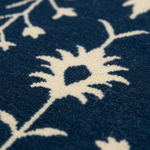 Close-up of a textured rug featuring a deep navy blue background with a cream-colored floral and vine pattern.