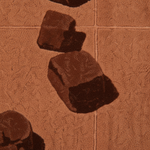 A close-up of a textured terracotta or rust-brown surface with dark brown stone-like shapes scattered on top, resembling a rug, mat, or textured print.