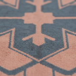 Close-up of a textured rug with a geometric pattern in dusty blue and muted peach-pink, showing the pile texture and sharp focus on the central motif.