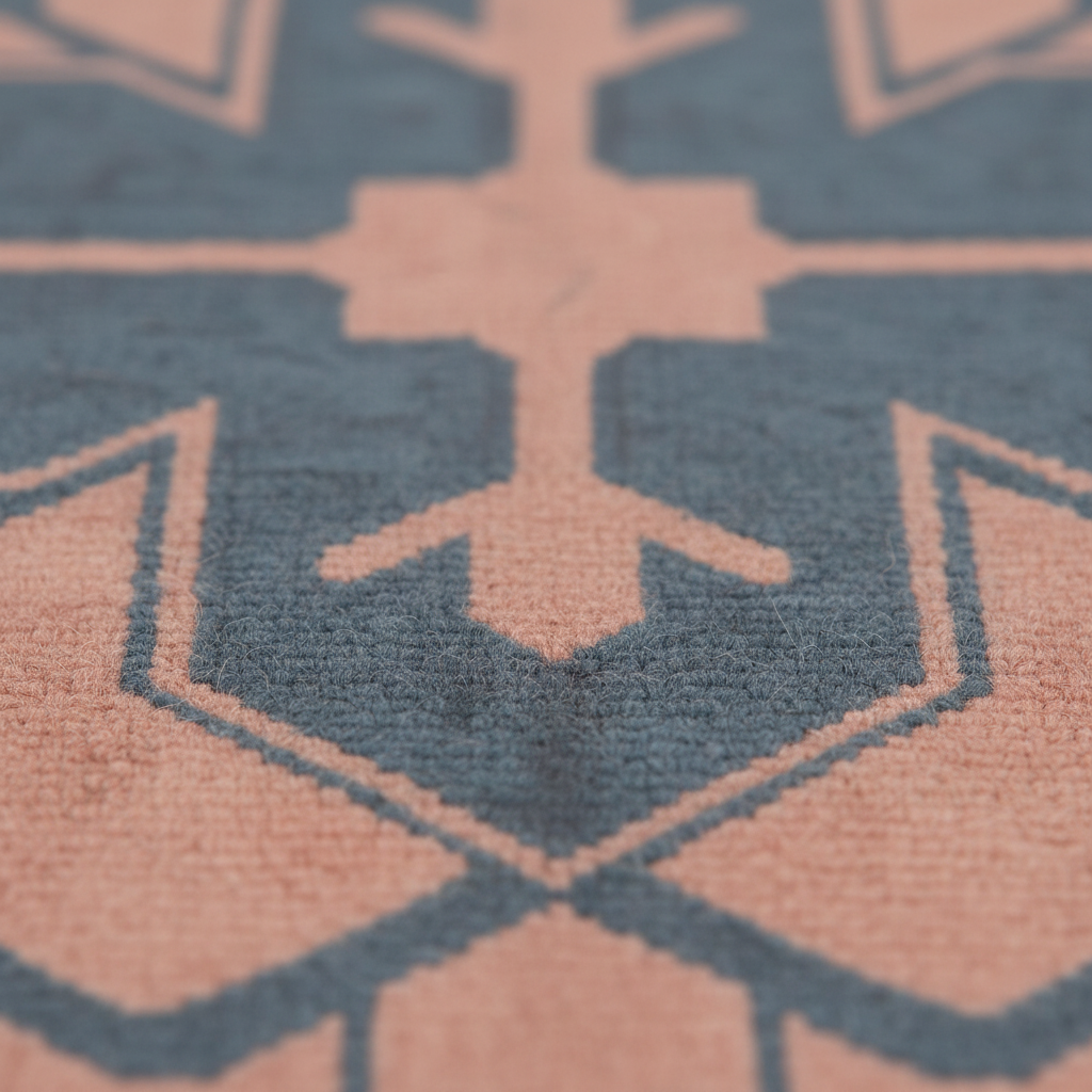Close-up of a textured rug with a geometric pattern in dusty blue and muted peach-pink, showing the pile texture and sharp focus on the central motif.