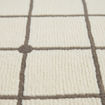 Close-up of a textured area rug with a cream-colored tufted surface and a taupe grid pattern.