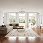 A bright, modern living room with a light beige sectional sofa, a wooden coffee table, a large cream checkered area rug, a hanging wicker chair, and a crystal chandelier over herringbone wood floors.