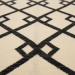 Close-up of a textured rug with a black geometric diamond lattice pattern on a warm cream background.