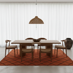 Dining area with wooden table and chairs on a terracotta rug, white walls, and a hanging woven lamp.