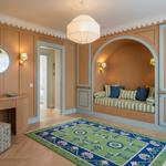A beautifully styled interior room with warm wood paneling, a built-in daybed with striped cushions, a green and blue patterned rug, and a white pendant light.