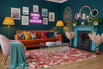 Modern living room with orange sofa, pink chair, red rug, and decorative elements.