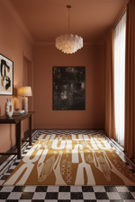 A large rectangular area rug with bold cream geometric and tribal-inspired patterns on a warm mustard-brown base, styled in a modern hallway with a black-and-white checkered floor, warm terracotta walls, and a white pendant light.