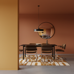 A modern dining room scene with a dark wood table, four brown upholstered chairs, a black pendant light, a round wall mirror, and a patterned rug in warm terracotta and mustard tones.