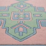 Close-up of a textured area rug with a geometric medallion pattern in pastel pink, sage green, and light blue.