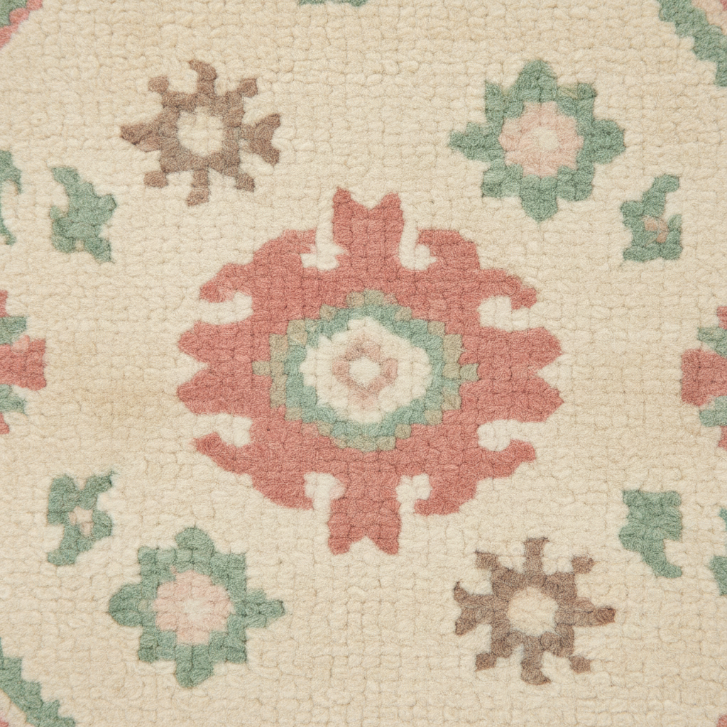 Close-up of a textured area rug featuring a central coral-red and sage green medallion surrounded by smaller floral motifs in muted brown, green, and pink on a cream background.