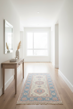 A long runner rug with a traditional medallion pattern in blue, beige, and rust tones, styled on a light wood floor in a bright, modern hallway with a console table and mirror.