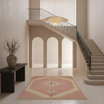 A rectangular area rug with a geometric medallion pattern in dusty pink and cream, styled on a light tile floor in a modern, minimalist staircase hallway.