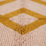 Close-up of a textured woven rug with a geometric diamond pattern in mustard yellow and pale blush pink.