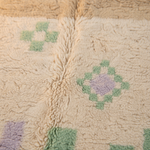 Close-up of a soft, textured fleece blanket with a cream base and geometric patterns in sage green and lavender purple.