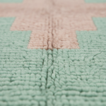 Close-up of a textured plush rug with a geometric pattern in mint green and pale pink.