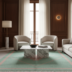 A modern living room scene featuring a mint green area rug with a pink geometric border, a white marble coffee table, two cream-colored armchairs, and dark wood paneling.