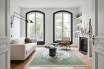 Living room with a green knotted floral rug, white sofa, and wooden chair.