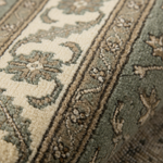 Close-up of a textured area rug with a traditional floral pattern in muted sage green, beige, and cream tones.