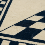 Close-up of a textured rug with a cream and dark navy geometric pattern, showing the pile texture and fine fibers.