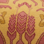Close-up of a textured area rug with a repeating ornamental floral or botanical pattern in dusty pink and mustard yellow.