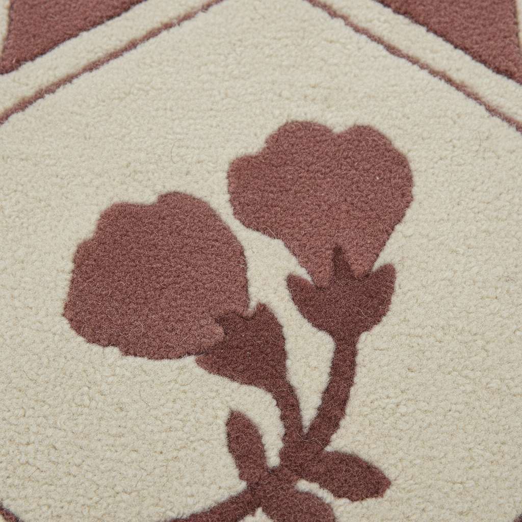 Close-up of a textured area rug featuring a cream-colored background with a stylized floral motif in a muted terracotta brown.