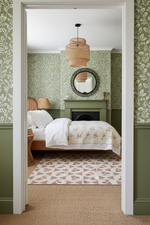 Bedroom with green walls, floral-patterned  rug, wallpaper, and a bed with white bedding.
