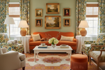 Living room with orange sofa, floral chairs, orange handmade rug, and decorative wall art.