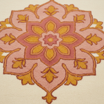 A close-up of a textured area rug featuring a symmetrical, ornate floral medallion pattern in shades of dusty pink, mustard yellow, and terracotta on a cream background.