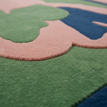 Close-up of a plush, high-pile area rug with a wavy, organic pattern in shades of green, dusty pink, and navy blue.