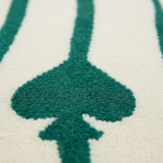 Close-up of a textured rug with a dark teal spade-shaped motif on a warm cream background.