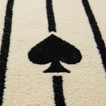 Close-up of a plush rug with a black spade symbol and vertical black stripes on a warm cream background.