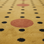 A close-up of a textured rug with a mustard yellow base, featuring a large dusty rose circle in the center and rows of black and rose-pink dots.
