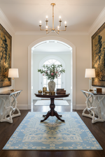 Elegant hallway with a chandelier, round table, and decorative blue rug.