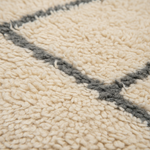 Close-up of a textured cream bouclé rug with a dark gray geometric border pattern.