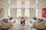 Luxurious living room with beige sofas, decorative rug, pillows, and a chandelier.