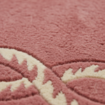 Close-up of a plush textured rug in dusty rose pink with a cream-colored abstract leaf or floral pattern.