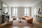 Modern living room with a curved pink sofa, pink traditional rug, white chairs, and a fireplace.