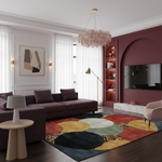 A modern living room interior featuring a large abstract-patterned area rug in navy, yellow, beige, and red tones. The room includes a dark purple sectional sofa, a pink armchair, a round wooden side table with a white lamp, a gold floor lamp, a pink glass chandelier, and a deep burgundy accent wall with an arched niche containing shelves and a mounted TV.