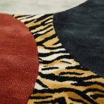 Close-up of a textured rug with a bold geometric pattern featuring a solid rust red circle, a black and tan tiger-stripe motif, and a dark charcoal section.