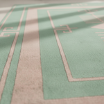 Close-up of a textured rug with a mint green and beige geometric pattern, featuring soft leaf shadows across the surface.