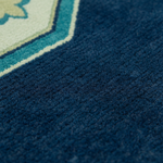 Close-up detail of a textured rug showing a deep navy blue field with a geometric border in teal, cream, and light blue.