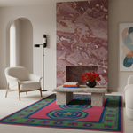 A colorful area rug with a pink, green, and blue geometric pattern is styled in a modern living room setting with a stone coffee table, white armchair, and a large pink marble fireplace wall.