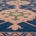 A close-up of a patterned rug with a deep blue background, peach-beige geometric medallions, and sage green central motifs.