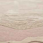 Close-up of a soft textured fabric or rug in blush pink and cream with wavy, layered ridges.