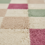 Close-up of a soft plush rug with a checkered pattern in cream, beige, dusty pink, and sage green.