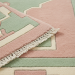 Close-up of a patterned rug with soft pink, sage green, and cream geometric sections and white fringe along one edge.